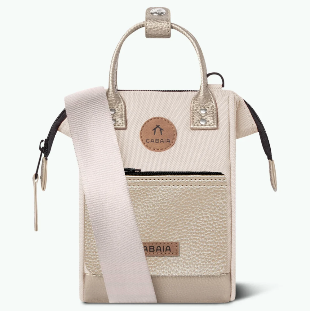 A small structured handbag in light beige pebbled canvas with a pale blush pink shoulder strap, a circular tan leather logo patch reading CABAIA, and a front zip pocket, shown on a clean white background.