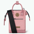 A pink velvet handbag with a black shoulder strap, featuring a top handle, front zip pocket, and a round brand patch that reads CABAIA.