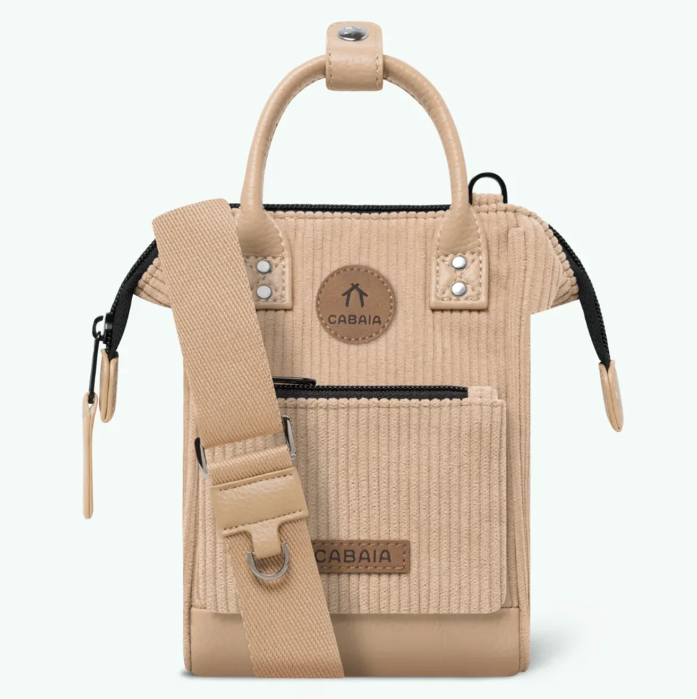 A beige velvet crossbody bag with dual top handles, a front zip pocket, and an adjustable shoulder strap, shown on a clean white background. The brand name 'CABAIA' is visible on a circular patch and a front label.