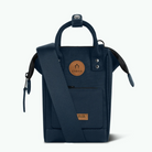 A navy blue Cabaia tote bag with a top handle, adjustable shoulder strap, front zip pocket, and two circular tan leather brand patches, shown on a clean white background.