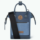 A blue Cabaia shoulder bag with a black adjustable strap, featuring a circular tan logo patch on the front pocket with the brand name CABAIA.