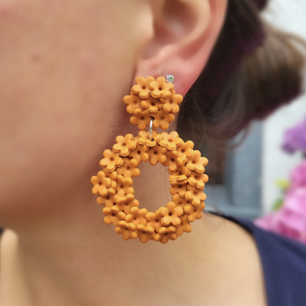 Close-up of a person wearing orange floral hoop earrings with a blurred background.