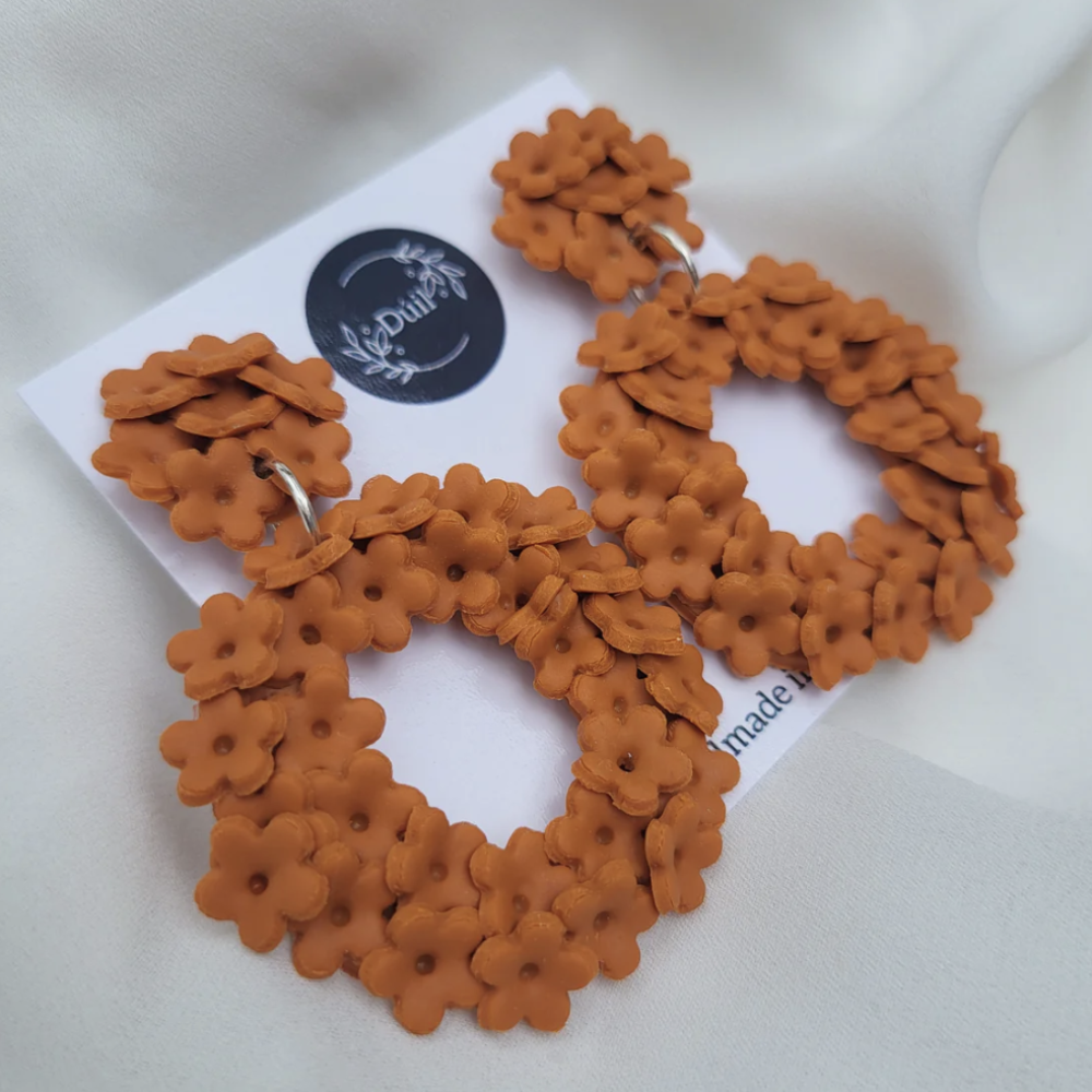 Pair of orange floral hoop earrings on a white card with 'Duil' branding.
