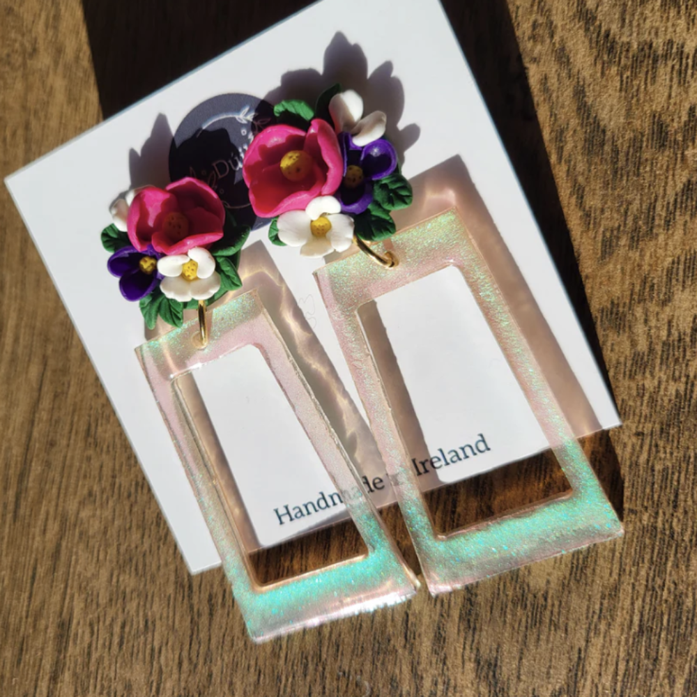 Pair of earrings with floral design on a card with 'Handmade in Ireland' text, placed on a wooden surface.