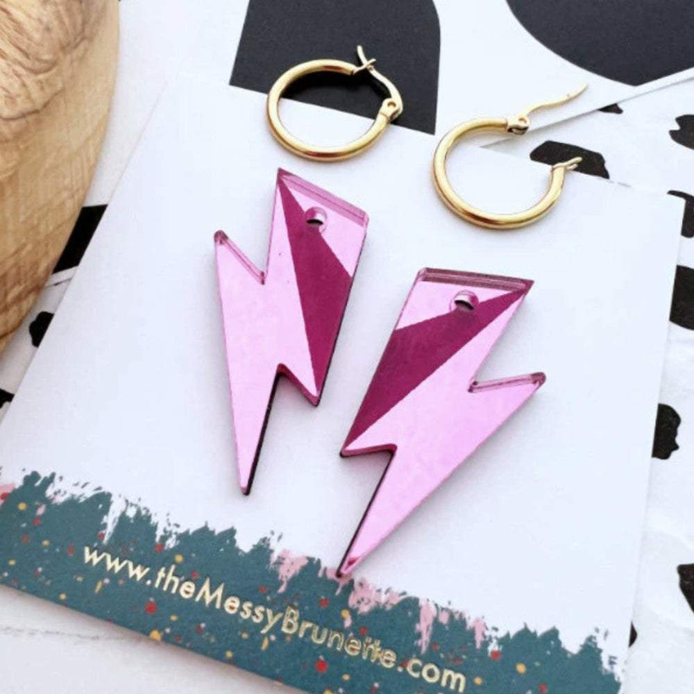 Pink lightning bolt earrings on a branded card with a black and white abstract design.
