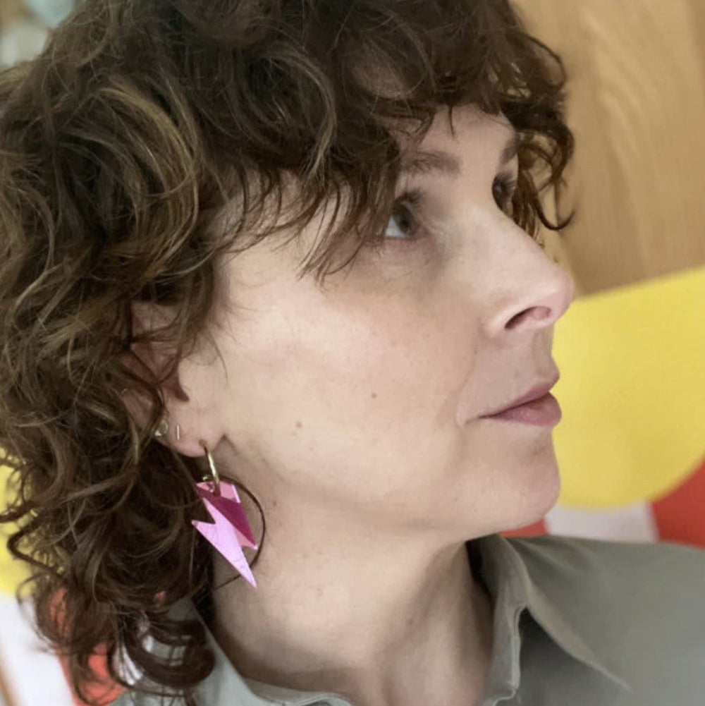 Woman with curly hair wearing a light-colored shirt and colorful earrings.