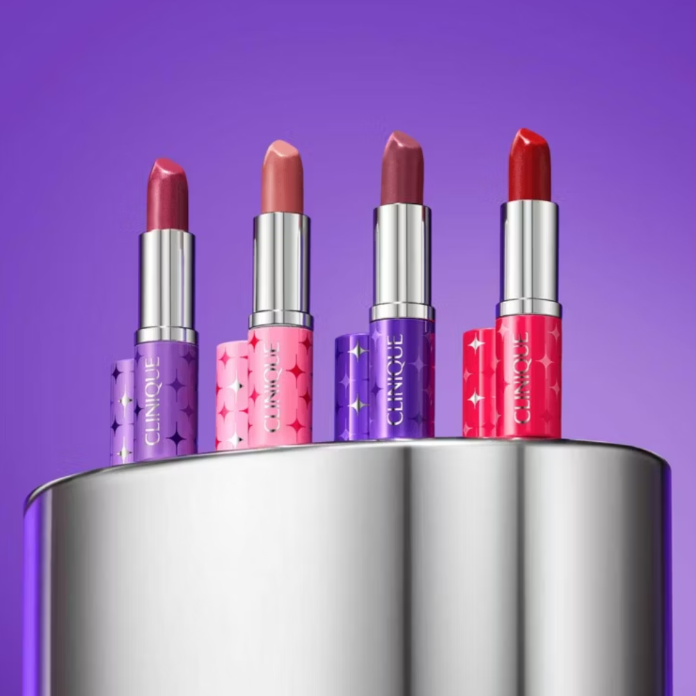 Four lipsticks in different shades on a metallic stand against a purple background