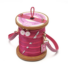 A pink spool-shaped handbag with faux leather stitching, silver zipper details, decorative buttons, and a hanging charm, photographed on a white background.