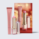Estée Lauder Beauty Collection lip and cheek care set, featuring a pink tube of Futurist Blush, and a pink tube of Lip Balm arranged in front of a red and gold branded backdrop card.