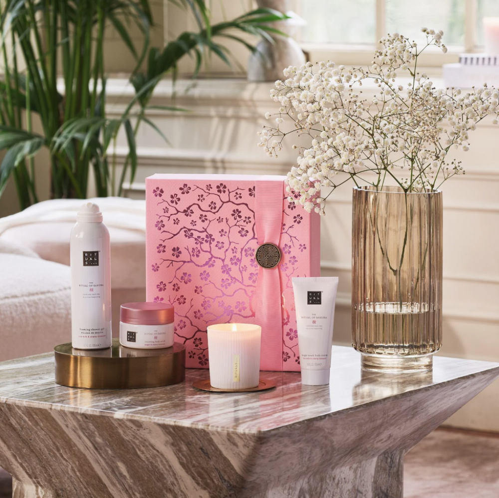 Cosmetic products and a pink book on a marble table with a plant in the background