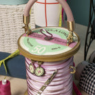 Spool of pink thread with a decorative handle, surrounded by sewing tools.