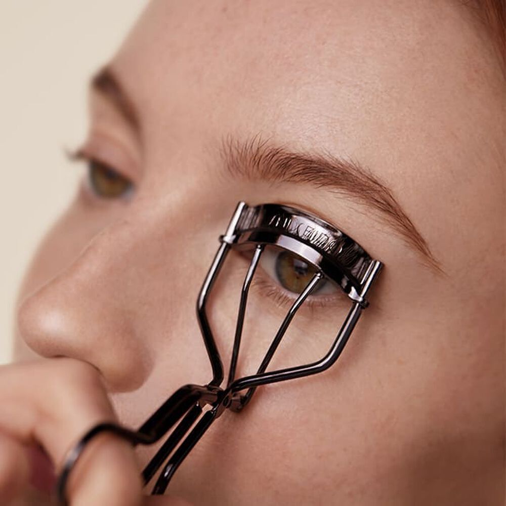 Eyelash curler being used on a person's eye with a neutral background