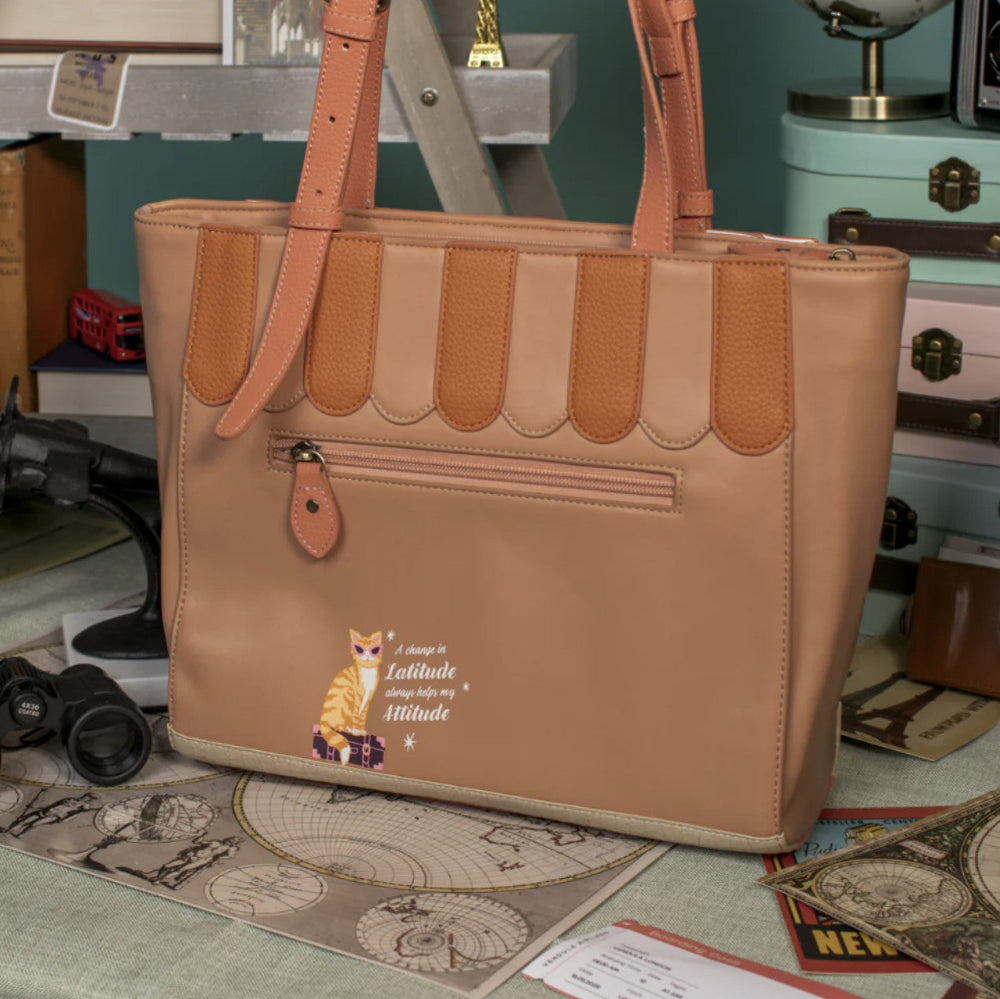 Brown handbag with a cat illustration on a surface with various items in the background