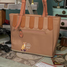 Brown handbag with a cat illustration on a surface with various items in the background