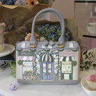 Handbag with a decorative design of shop fronts on a table with flowers and cupcakes.