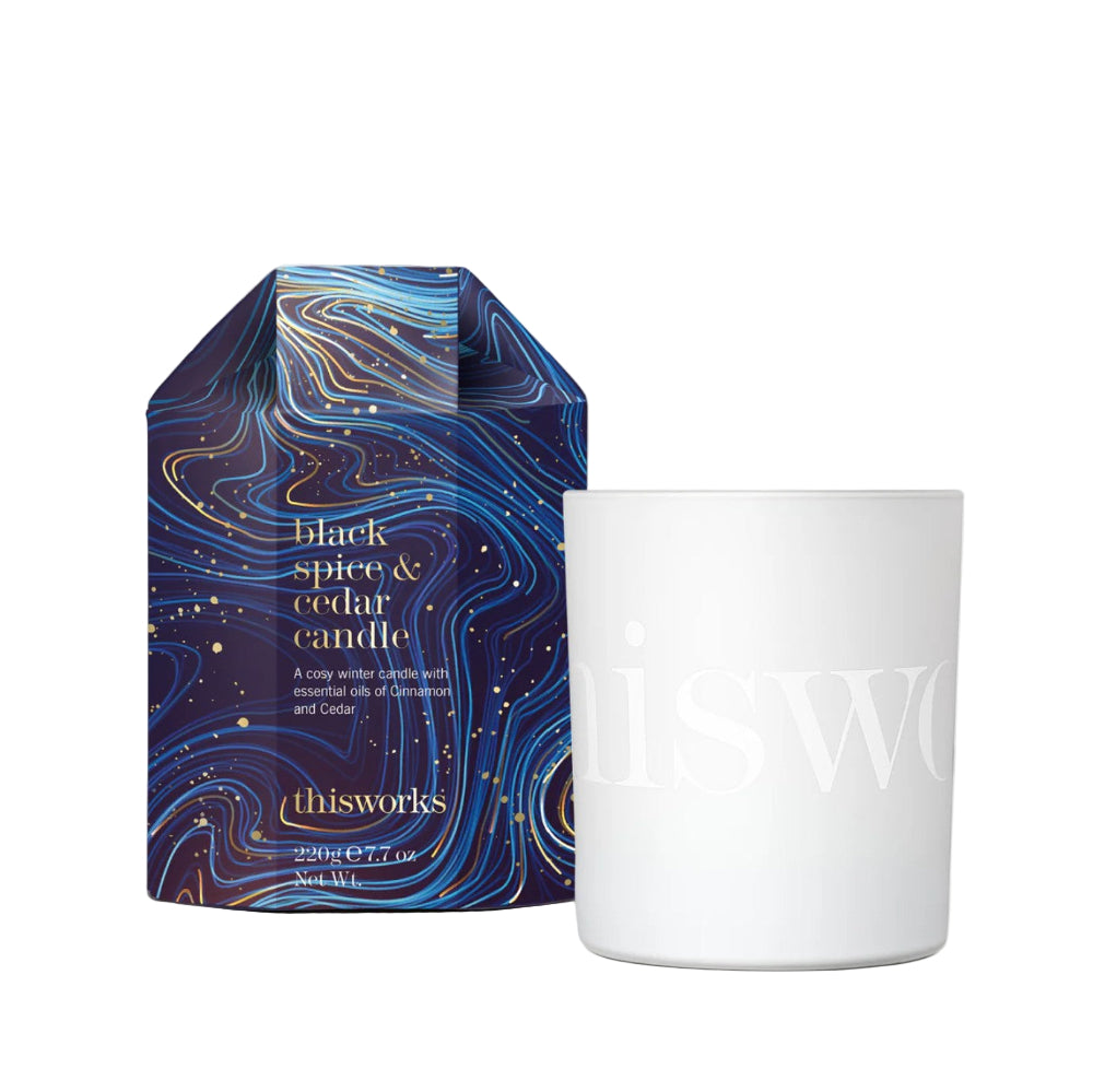 White candle with 'thisworks' branding next to a blue marbled box labeled 'black spice & cedar candle'.