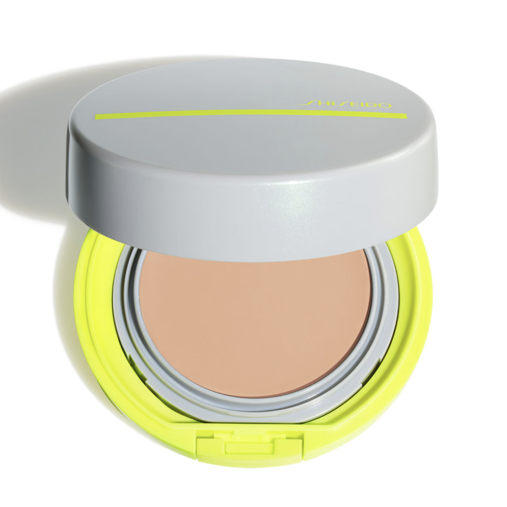 An open round cushion foundation compact with a light gray lid, a bright neon yellow-green base, and a beige pressed powder foundation pan visible inside, shown on a white background with a soft shadow.