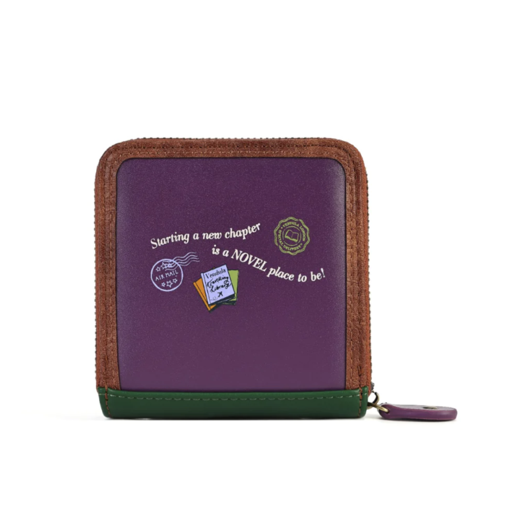 A purple zip-around wallet with brown textured trim, a green base trim, and white text reading 'Starting a new chapter is a NOVEL place to be!' with small decorative badges, shown on a white background.