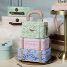 Stack of pastel-colored suitcases with floral and chain patterns on a decorative surface.