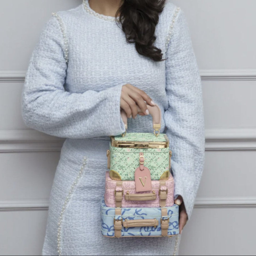 Woman holding a colorful handbag against a light gray wall with abstract art in the background.