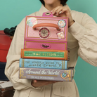 Person holding a decorative book set bag with travel-themed design against a teal background