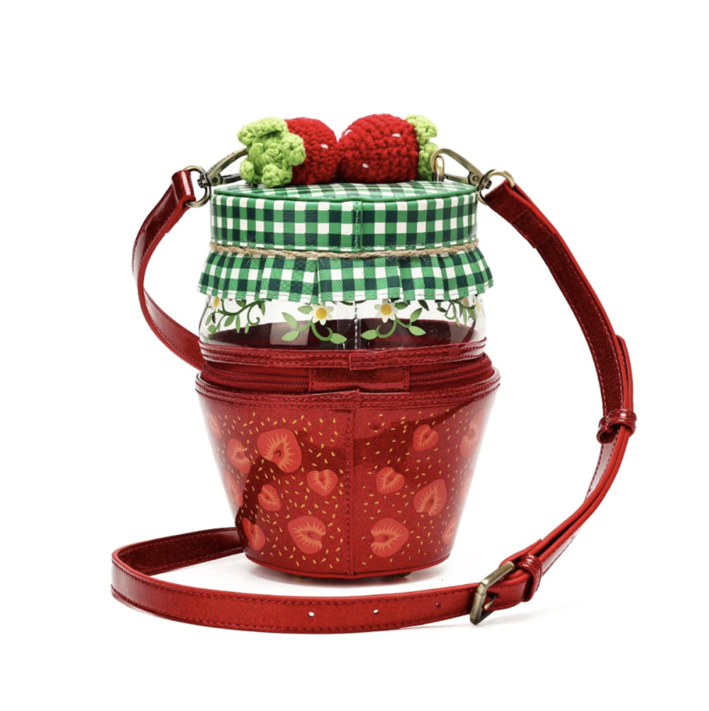 A strawberry-themed shoulder bag designed like a jar of jam, featuring a red body with strawberry prints, a green and white checkered lid, a clear glass jar section with floral detailing, and two crocheted strawberries on top, shown on a white background with an adjustable red strap.