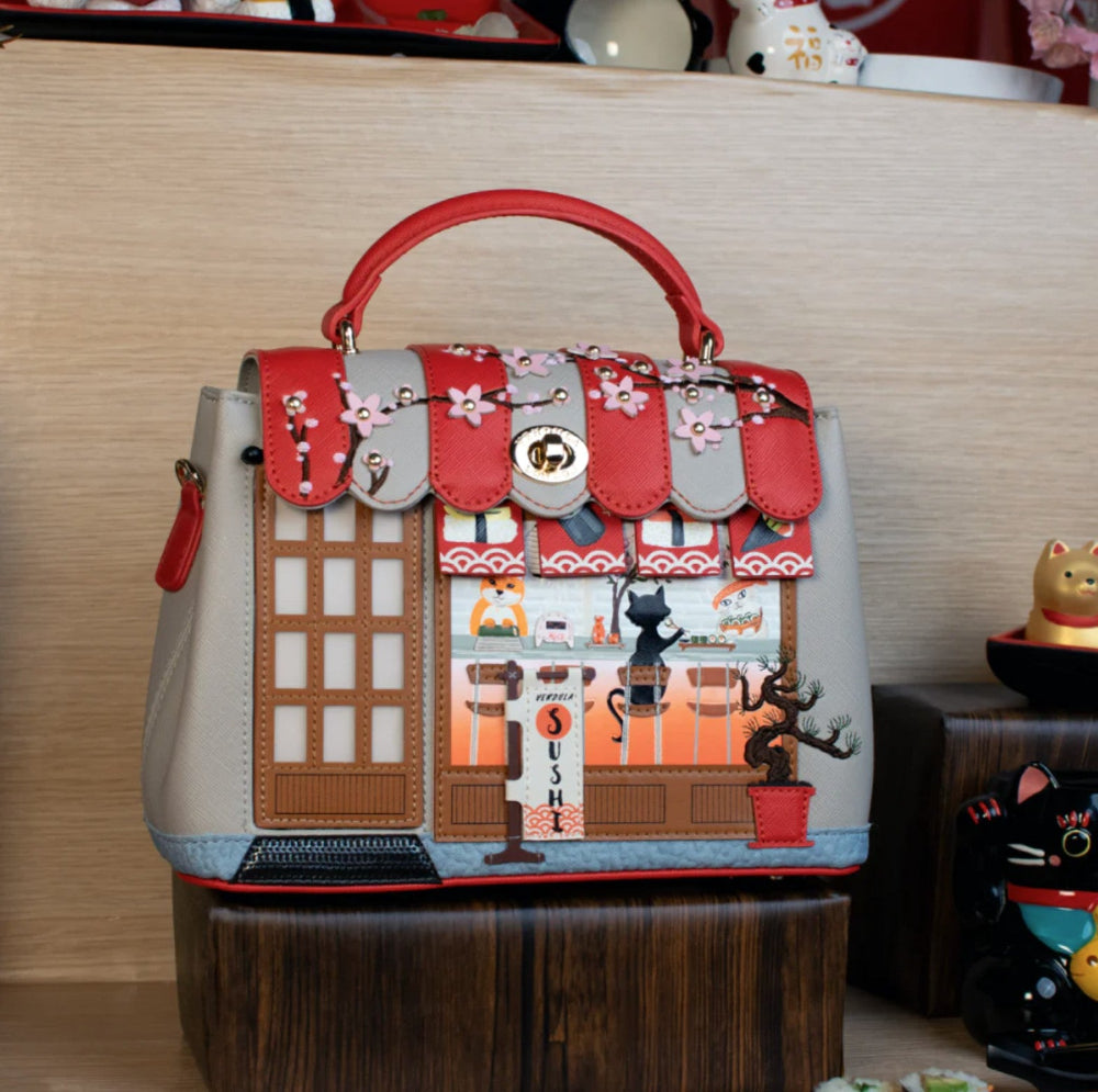 Handbag with a detailed design of a building and cats on a wooden surface.
