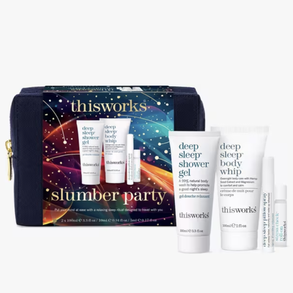 Thisworks Slumber Party gift set featuring a navy blue zippered cosmetic pouch with a colorful cosmic print, alongside four white skincare products: deep sleep shower gel, deep sleep body whip, deep sleep pillow spray, and roller