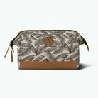 A rectangular zippered pouch with a beige and brown tropical leaf print, featuring a solid brown faux-leather bottom panel and a circular brown brand patch on the front.