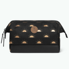 A black cosmetic pouch with a repeating metallic gold sunburst pattern, featuring a circular brown leather brand patch in the center and a black textured bottom panel.