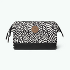 A rectangular cosmetic pouch with a black and white print pattern, a solid black base, and a circular brown leather logo patch on the front. The pouch is shown against a plain white background.