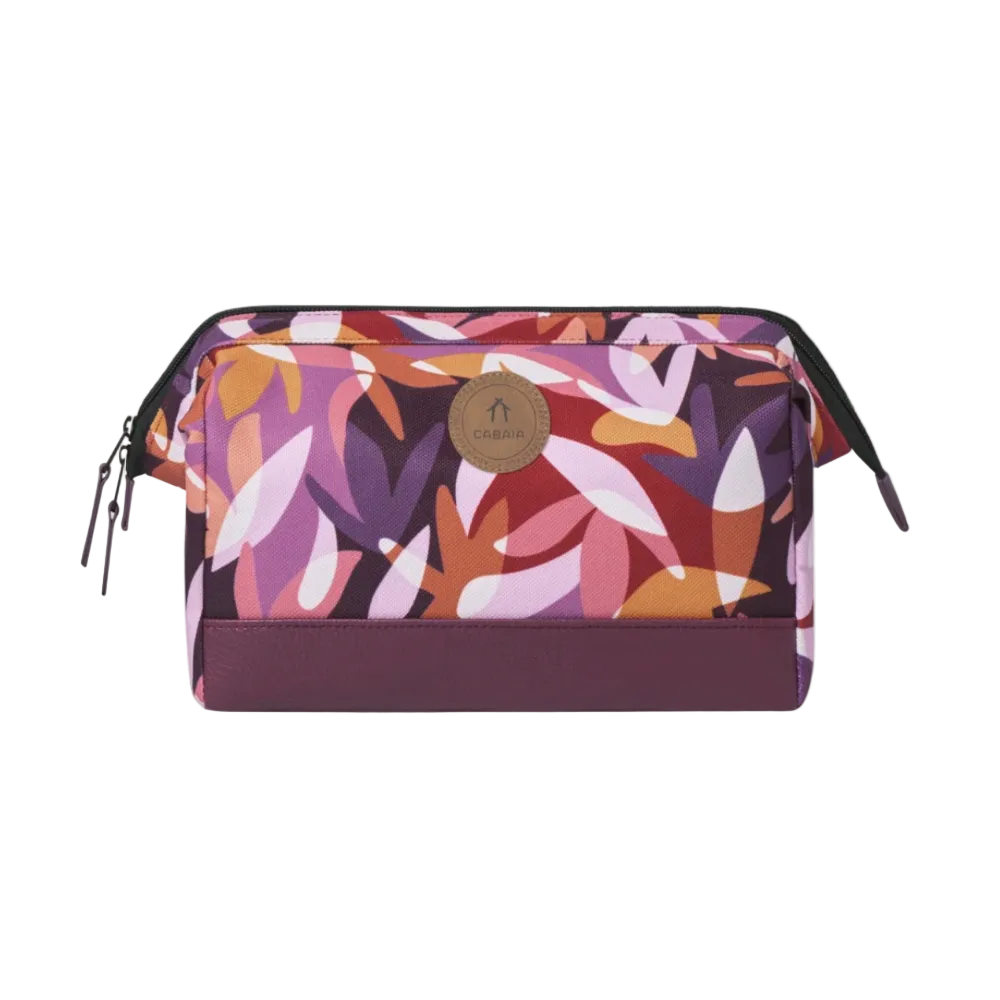 A rectangular zippered pouch with a colorful abstract leaf pattern in purple, pink, orange, and white, featuring a solid dark purple base and a circular brown leather brand patch on the front.