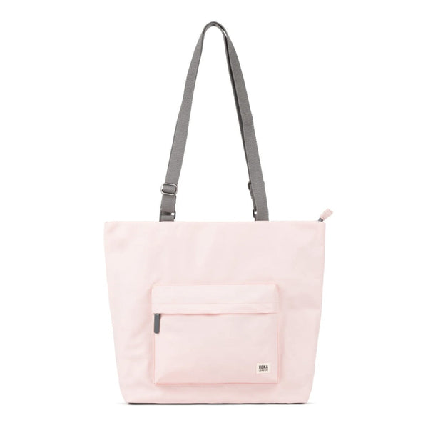 A light pink canvas tote bag with a grey adjustable shoulder strap and a front pocket.