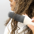 Person using a hairbrush on wet hair against a plain background