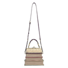A handbag designed to look like a stack of vintage books, featuring a textured cream and gold faux-croc pattern on the top book, a beige and pink striped middle book, and a pink striped bottom book, with a dark purple shoulder strap and gold-tone hardware, shown on a plain white background.