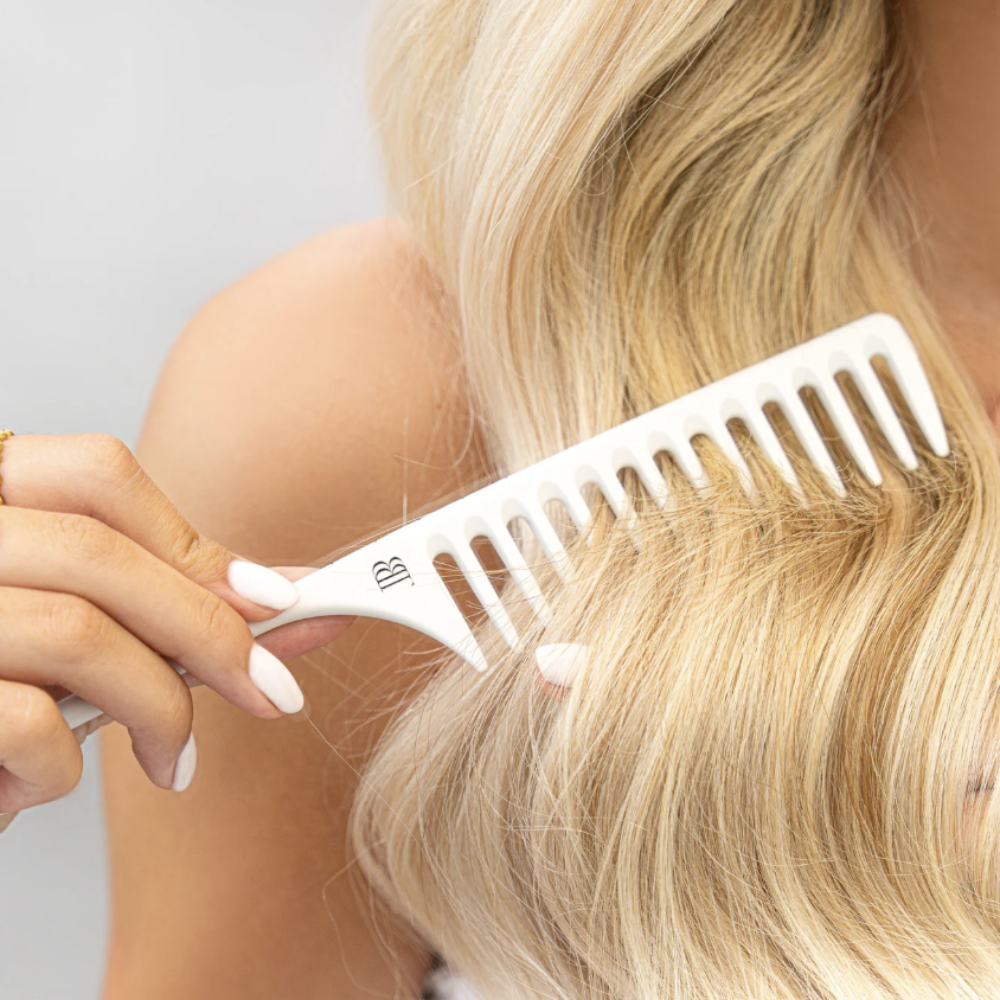 Person with blonde hair using a white comb on a light gray background