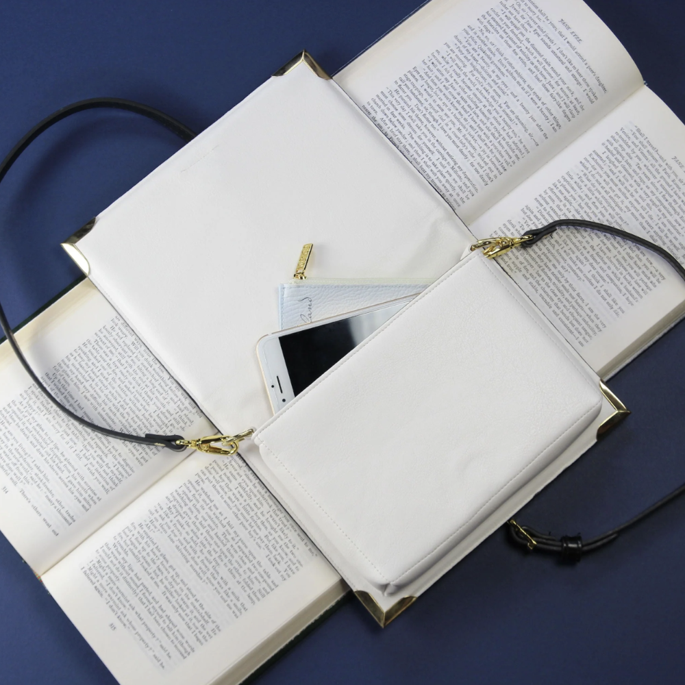 White handbag with gold accents on top of an open book