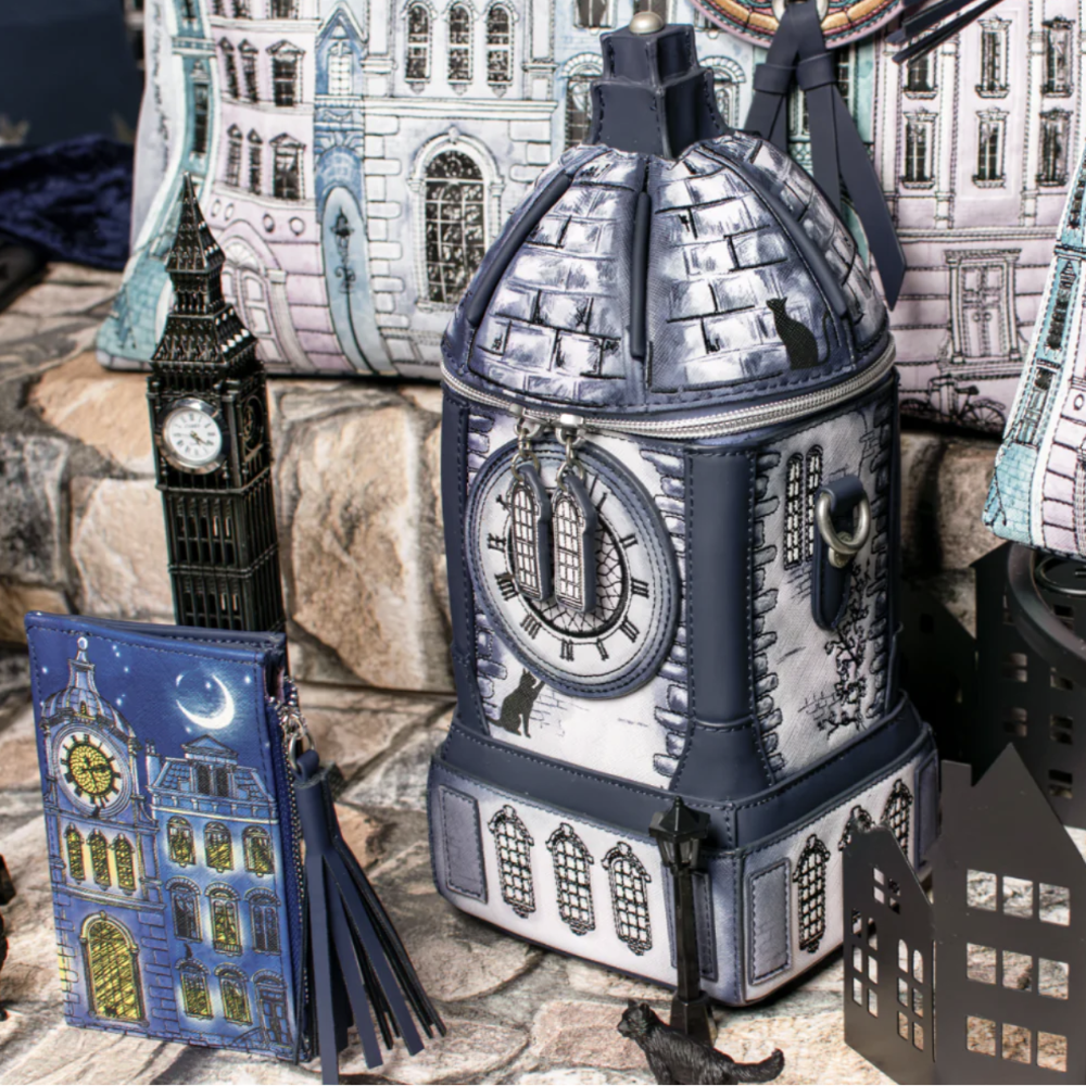 A gothic London-themed zippered bag shaped like Big Ben, displayed alongside matching zippered accessories including a blue clock-face notebook and a black cutout streetlamp on a stone surface.